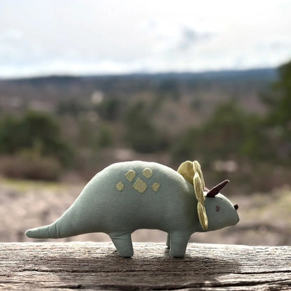 Plush dinosaur toy with a yellow hat on a wooden surface with a blurred natural background