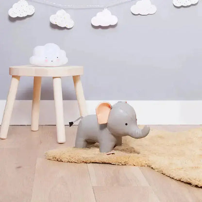 Gray elephant toy on a beige rug with a wooden stool and cloud-shaped object in a room.