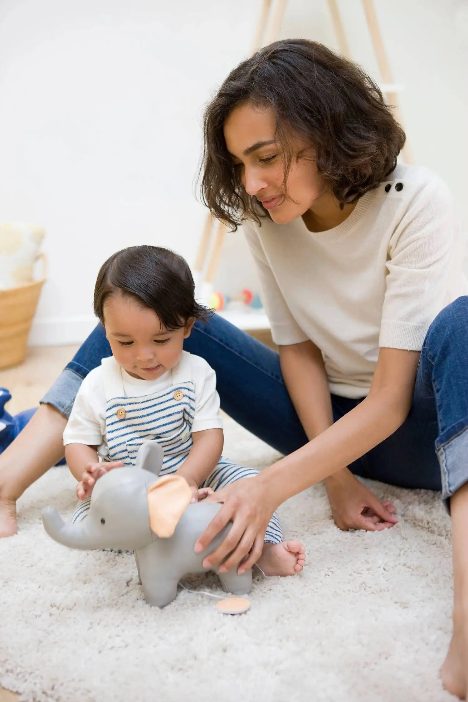 Woman and child playing with a grey elephant toy on a white carpet