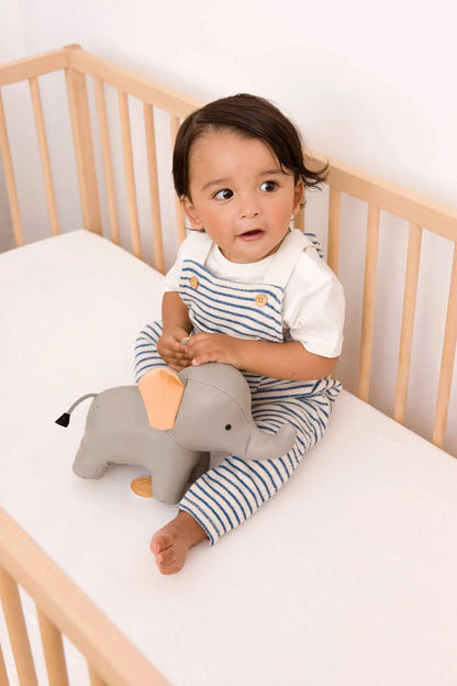 Child sitting in a crib with a plush elephant toy