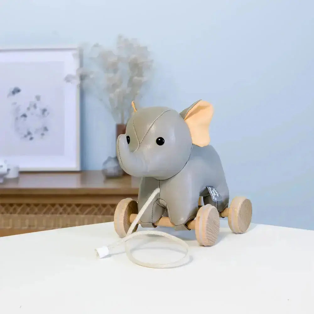 Grey elephant toy with wooden wheels on a white surface against a light blue wall.