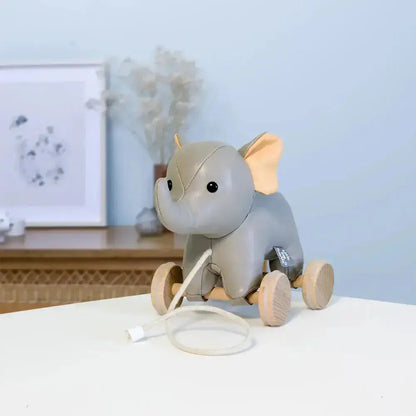 Grey elephant toy with wooden wheels on a white surface against a light blue wall.